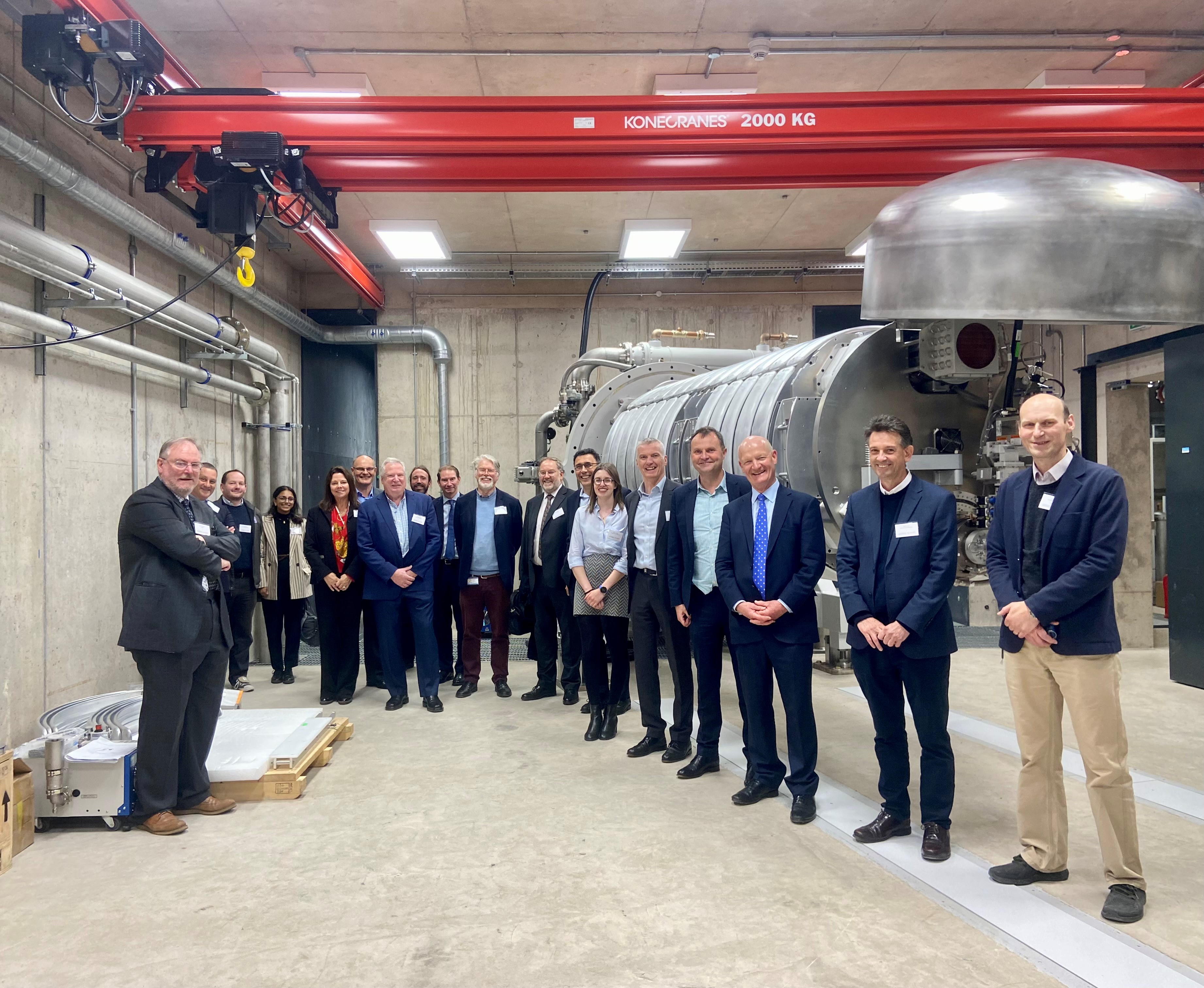 Scientists, Lord Willetts, and others, standing in front of the accelerator